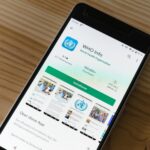 Mobile phone on wooden table showing installation screen for WHO Info app from World Health Organization.